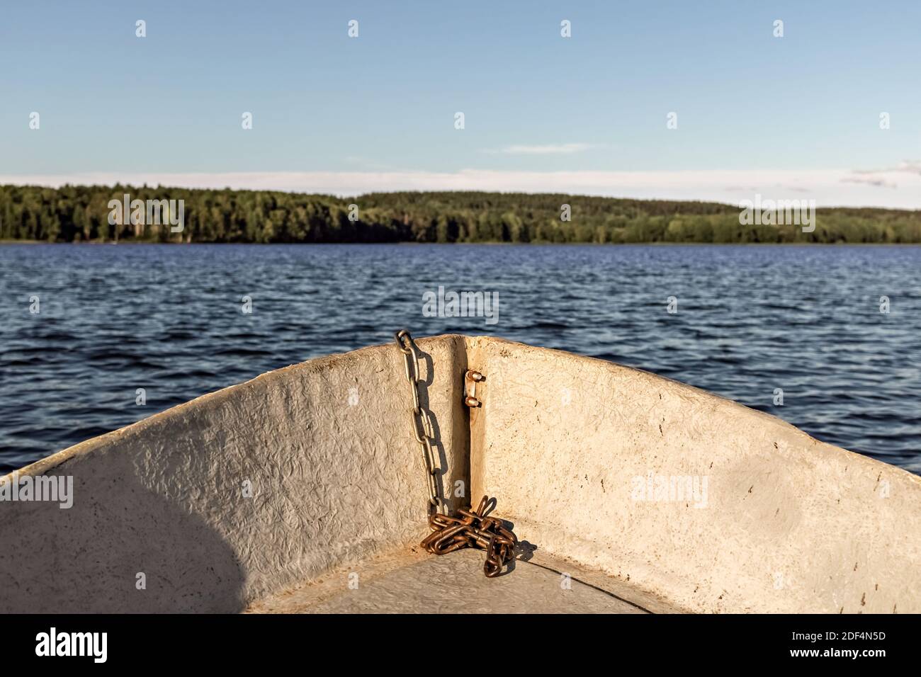 The photo was taken from a wooden boat, the bow of the boat with a chain is visible, in the background there is a blurred lake and shore. Stock Photo