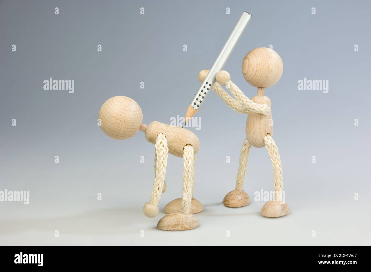 Zwei Holzfiguren, eine attackiert die andere mit einem Bleistift Stock Photo