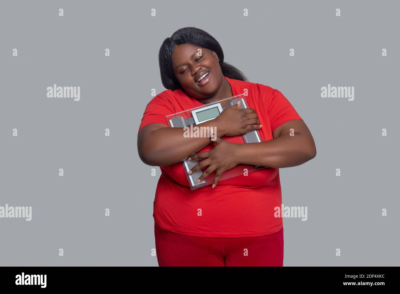 Young dark-skinned woman in red clothes holding weighing machine Stock Photo