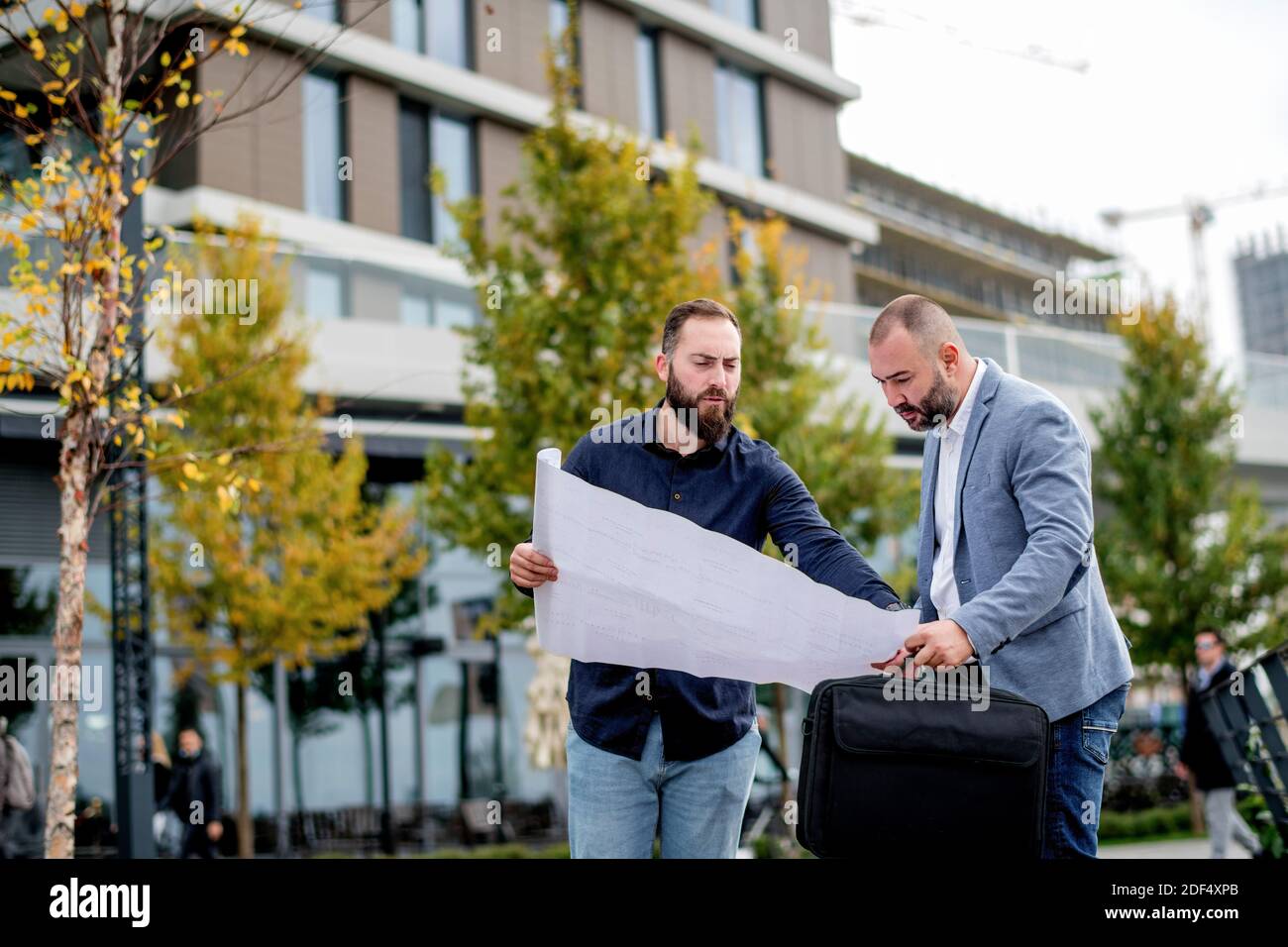 Two young engineers checking the architectural plan outdoors Stock Photo