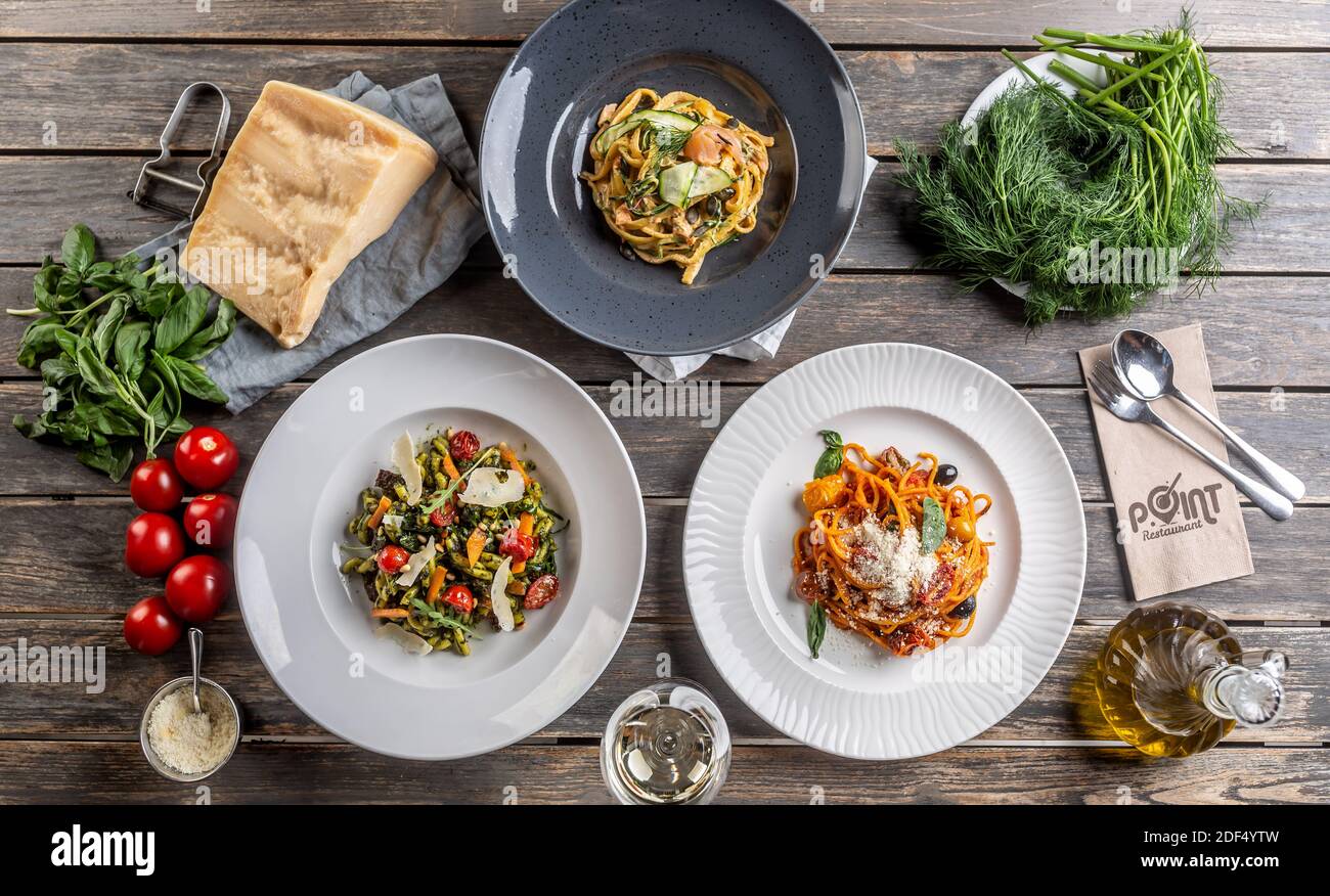 Top view of various pasta dishes served on plates, surrounded by ingredients on a vintage wooden surface. Stock Photo
