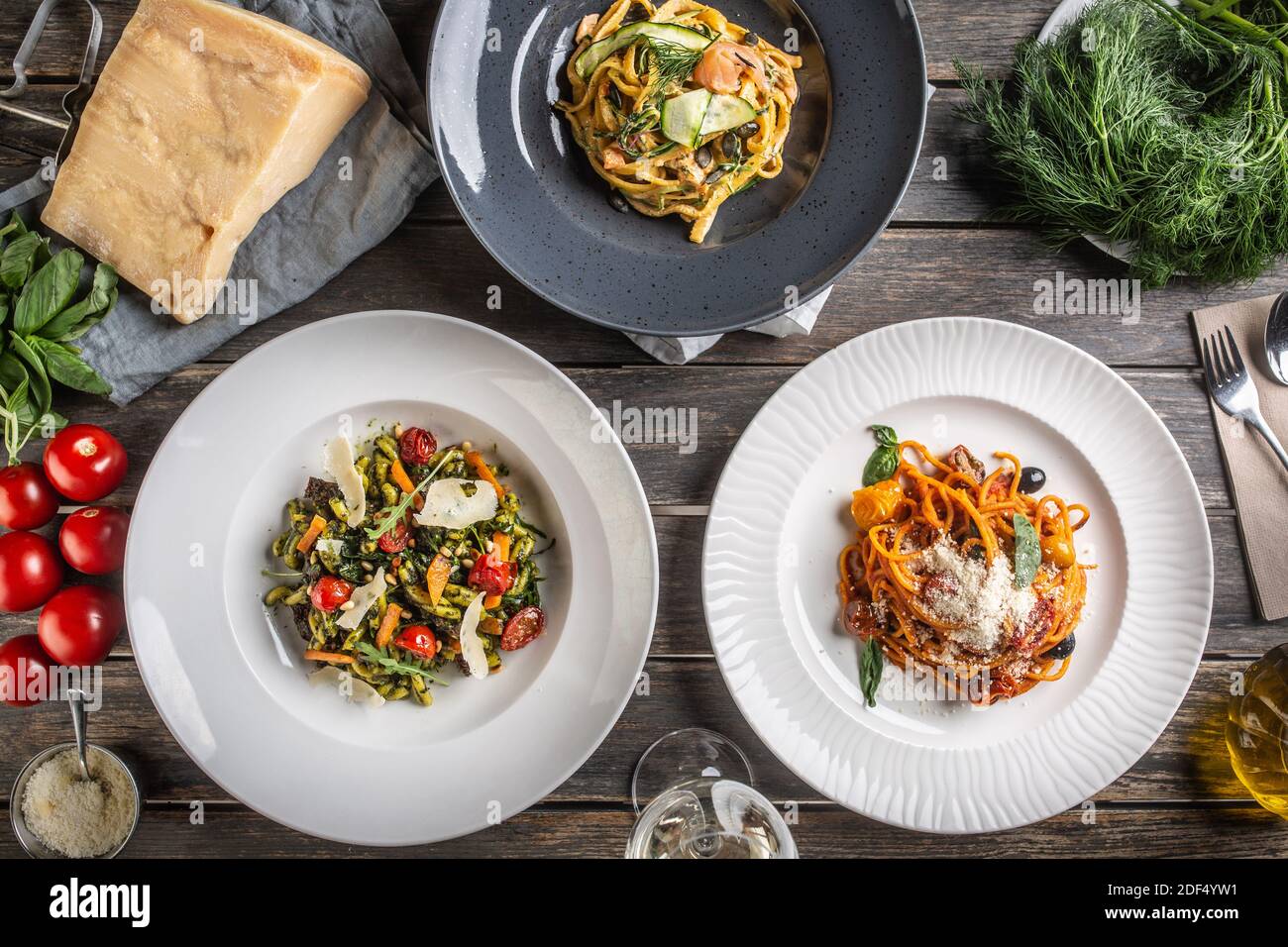 Top view of various pasta dishes served on plates, surrounded by ingredients on a vintage wooden surface. Stock Photo