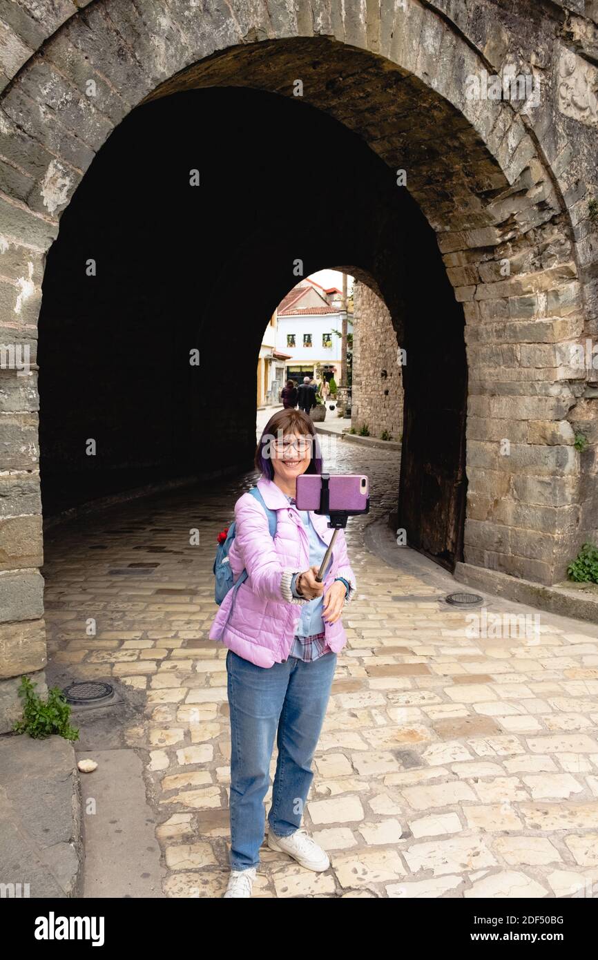 Beautiful Caucasian tourist woman taking a selfie with a selfie stick in Ioannina, Greece. Stock Photo