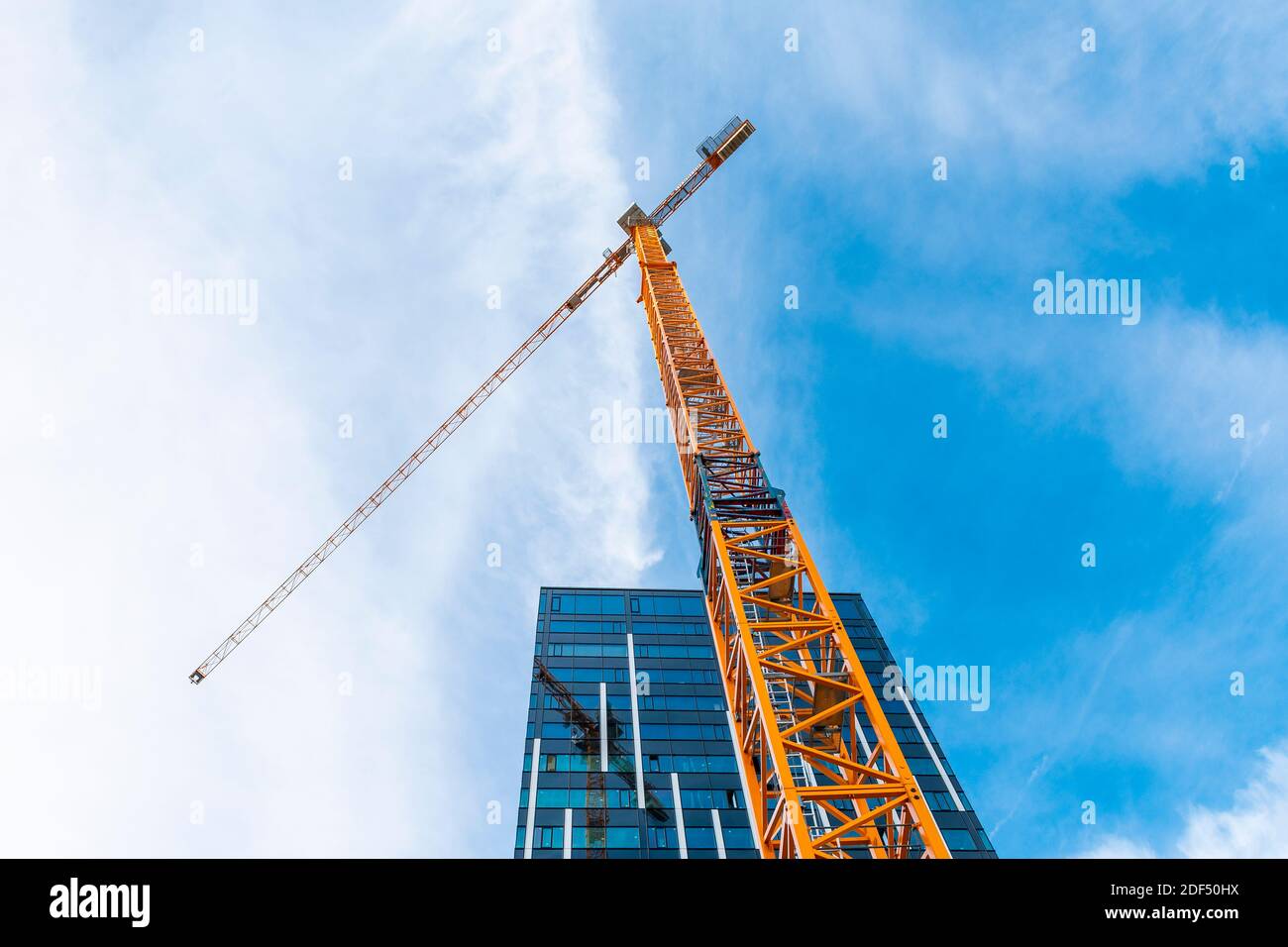 Yellow tower crane. Bottom view of a tall construction crane next to a modern building. Stock Photo