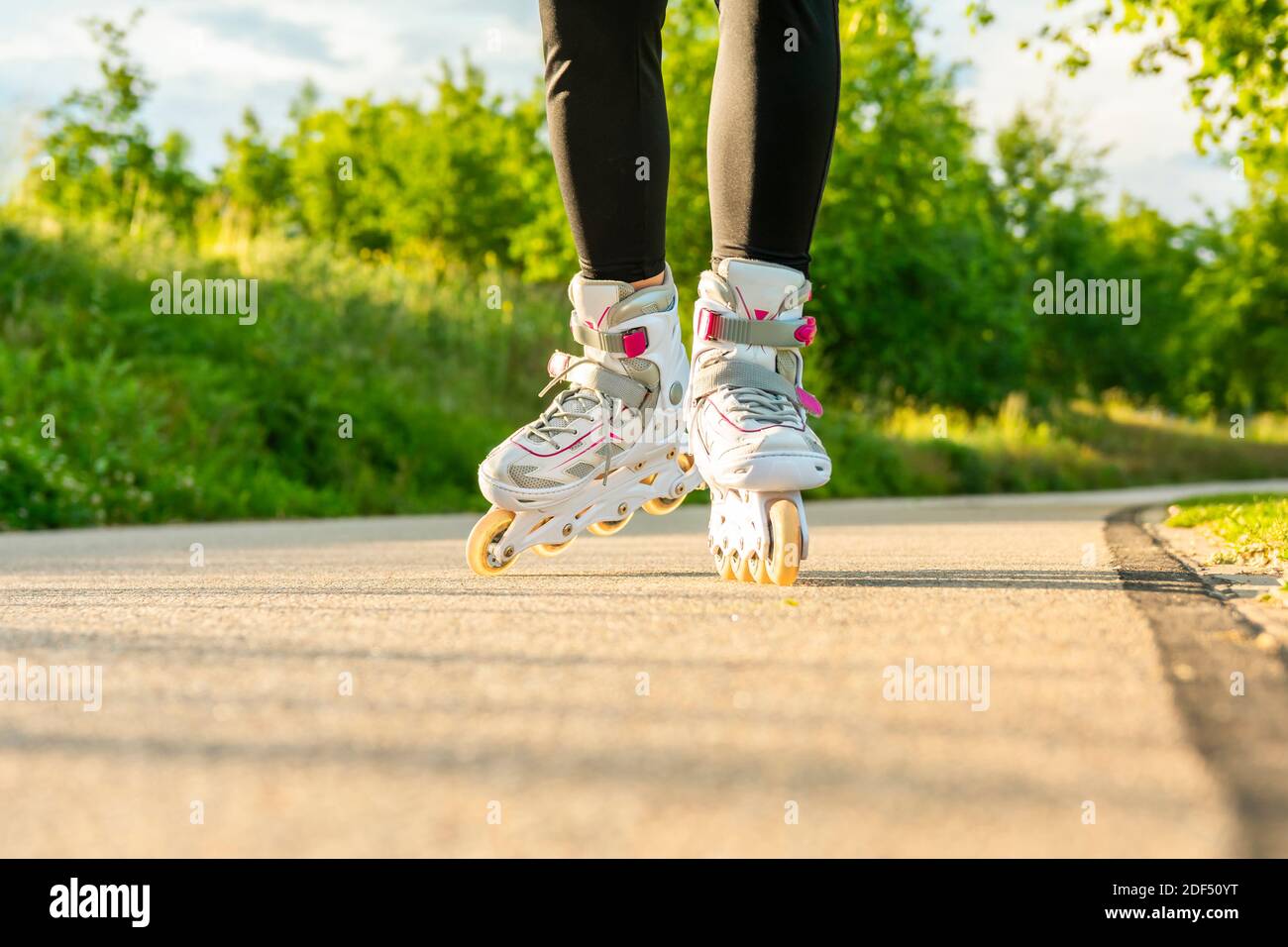 Woman's legs with white roller blades at sunny day on asphalt road. Stock Photo