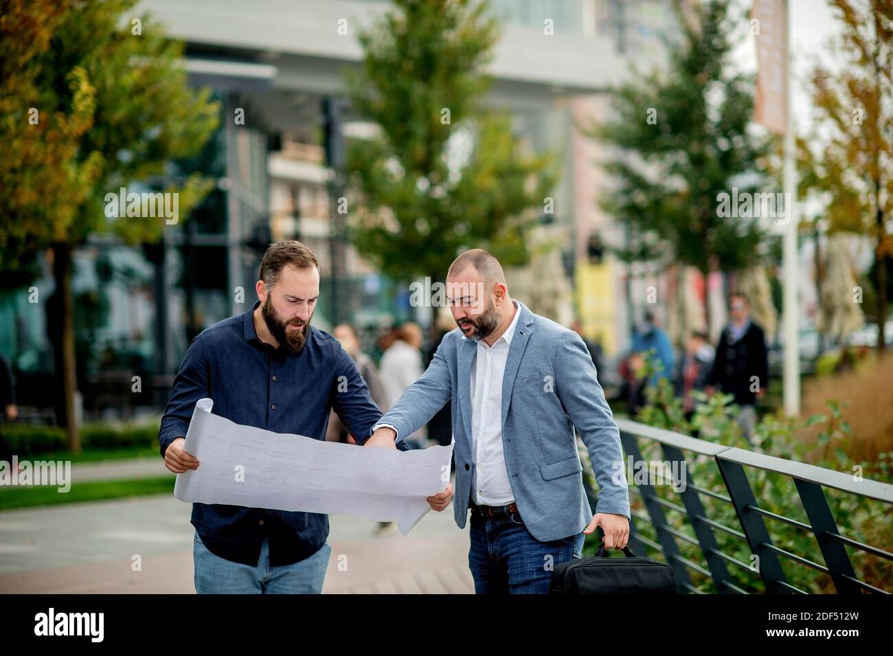 Two young engineers checking the architectural plan outdoors Stock Photo
