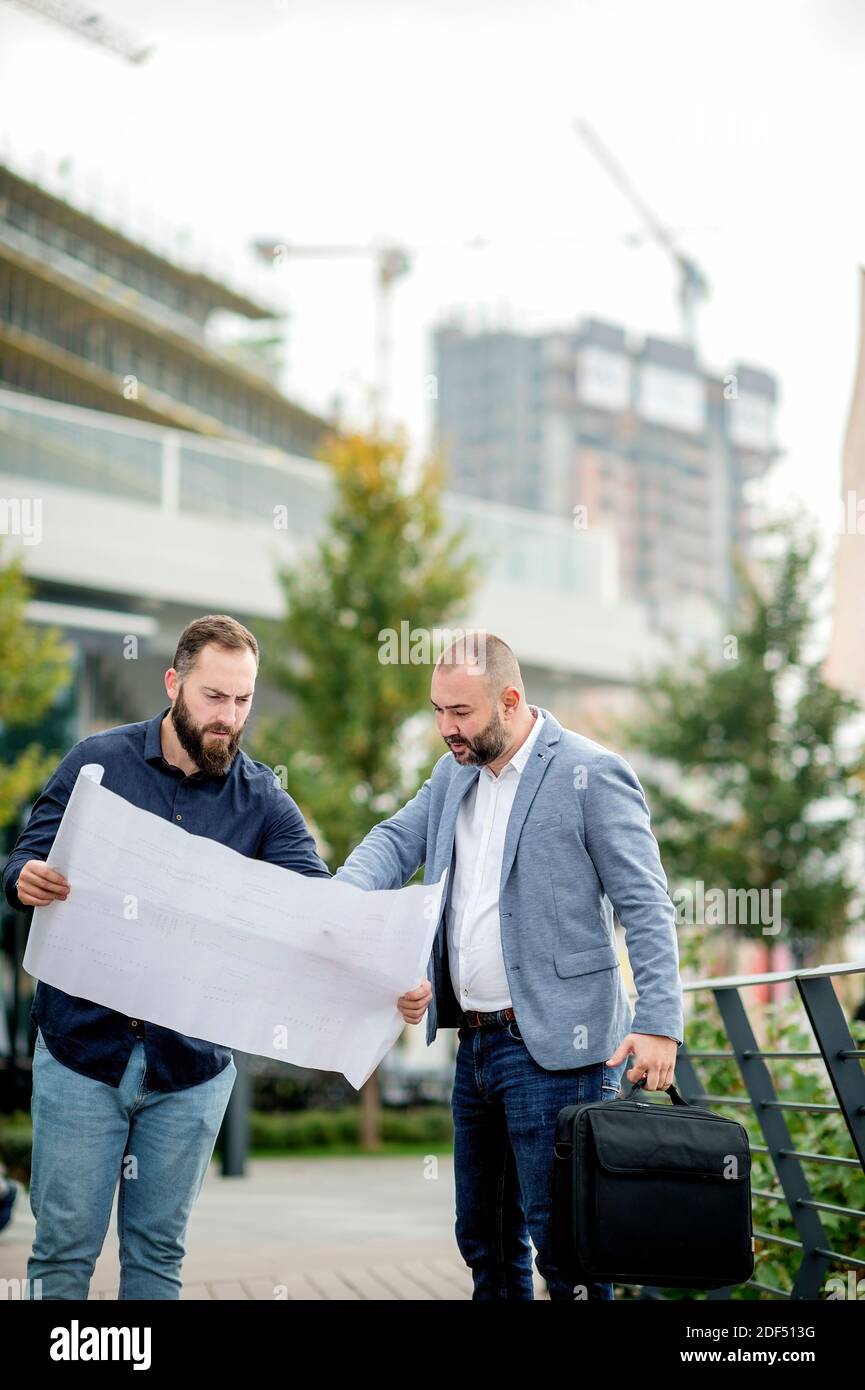 Two young engineers checking the architectural plan outdoors Stock Photo