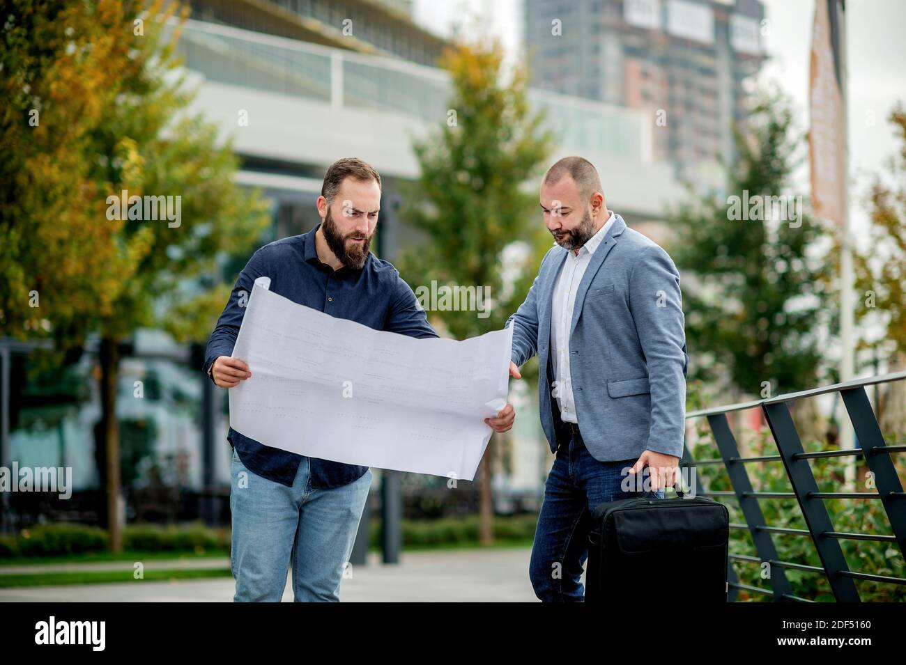 Two young engineers checking the architectural plan outdoors Stock Photo