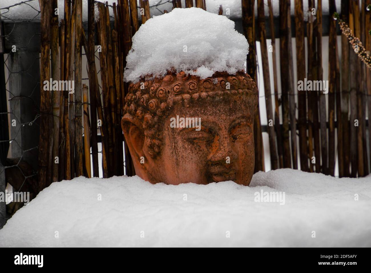 Old weathered terracotta buddha head covered with snow Stock Photo