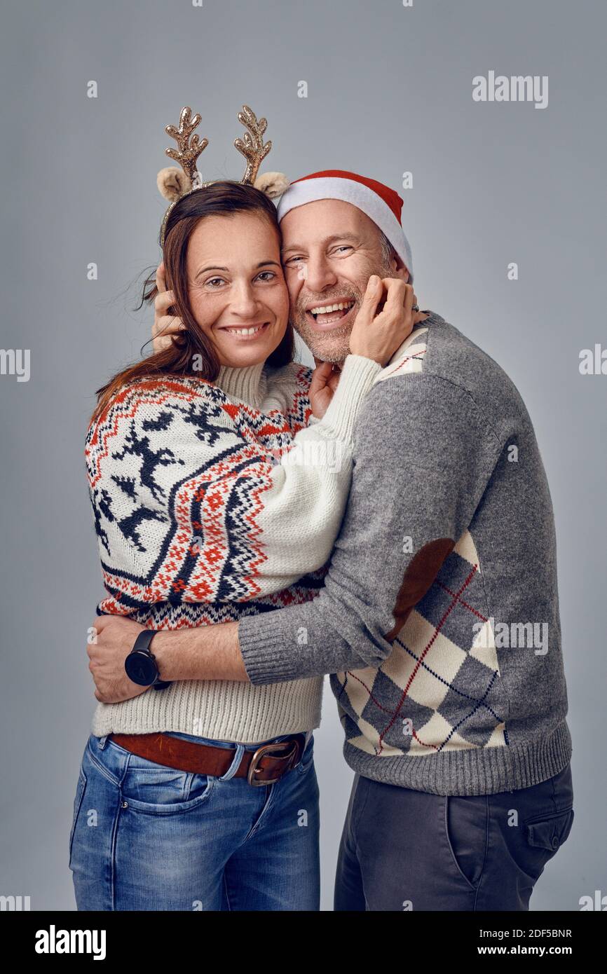 Middle-aged happy couple laughing and hugging each other wearing a santa hat and an elk headband Stock Photo