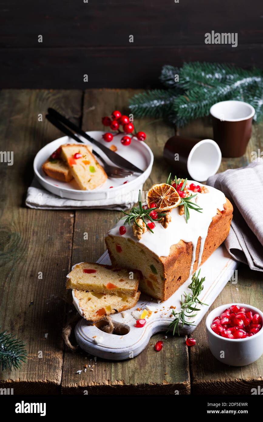 Fruit cake dusted sliced with icing, nuts, kernels pomegranate and dry orange close-up. Christmas and Winter Holidays homemade cake Stock Photo