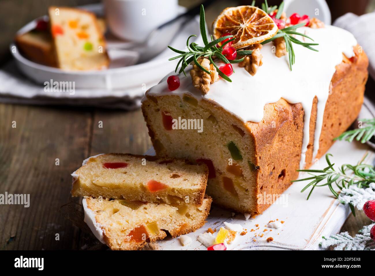 Fruit cake dusted sliced with icing, nuts, kernels pomegranate and dry orange close-up. Christmas and Winter Holidays homemade cake Stock Photo