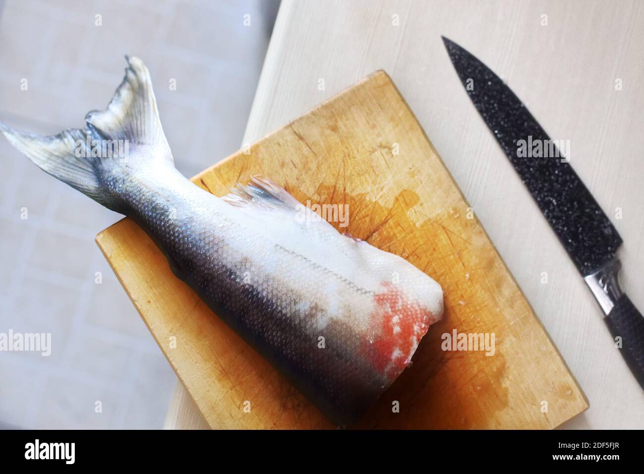 On the cutting Board is a piece of fish and a knife. The cooking process of the fish.  Stock Photo