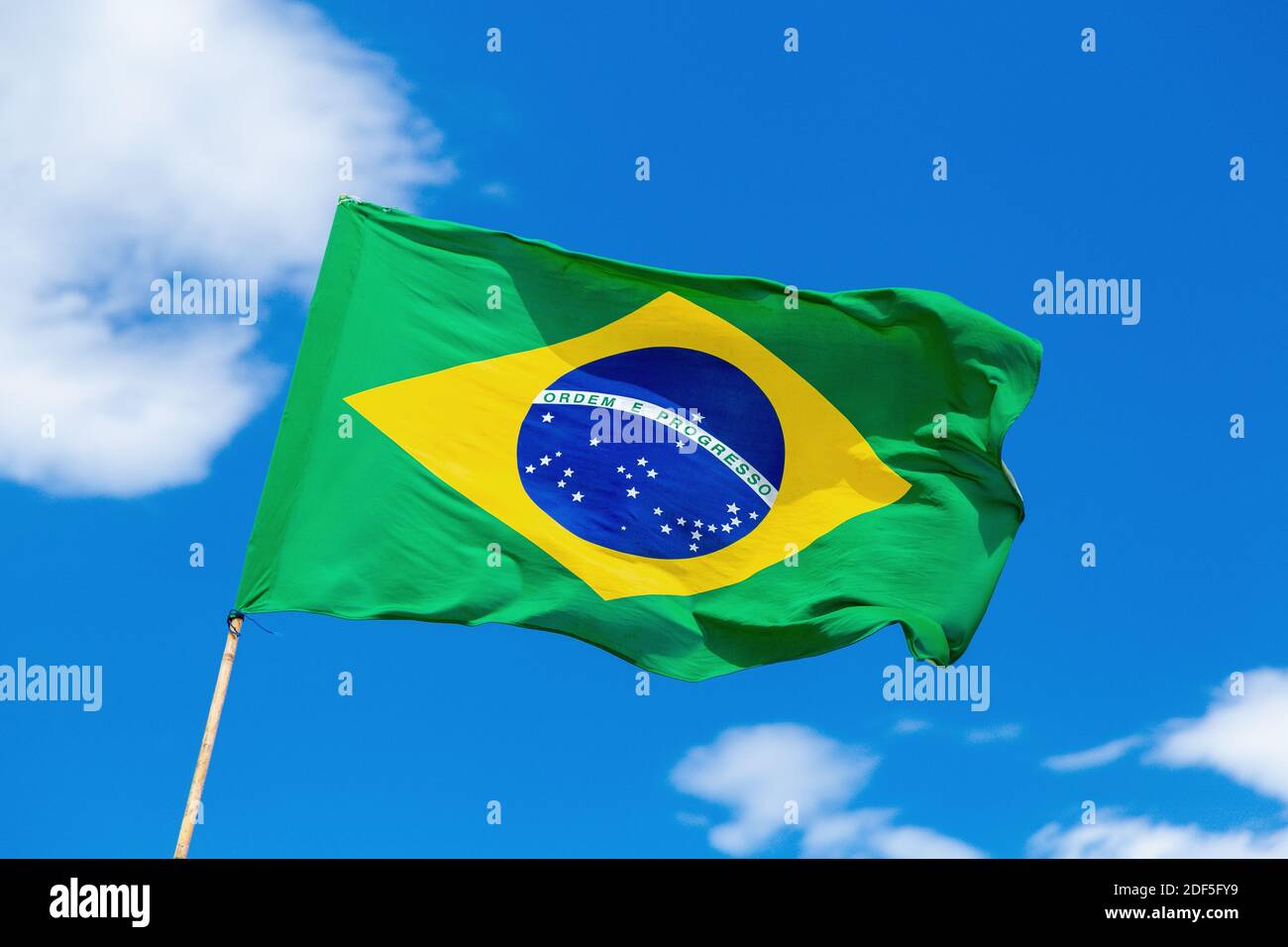 Brazilian flag waving on blue sky with some clouds. Brazil country colors. Stock Photo