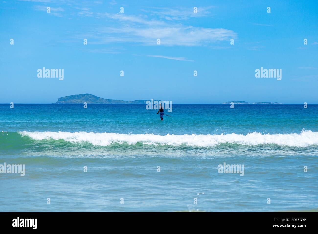 Stand up paddle boarding (SUP) in south atlantic coast. Isolated man doing aquatic sports in sunny day of summer. Geriba beach, Buzios, Rio de Janeiro Stock Photo