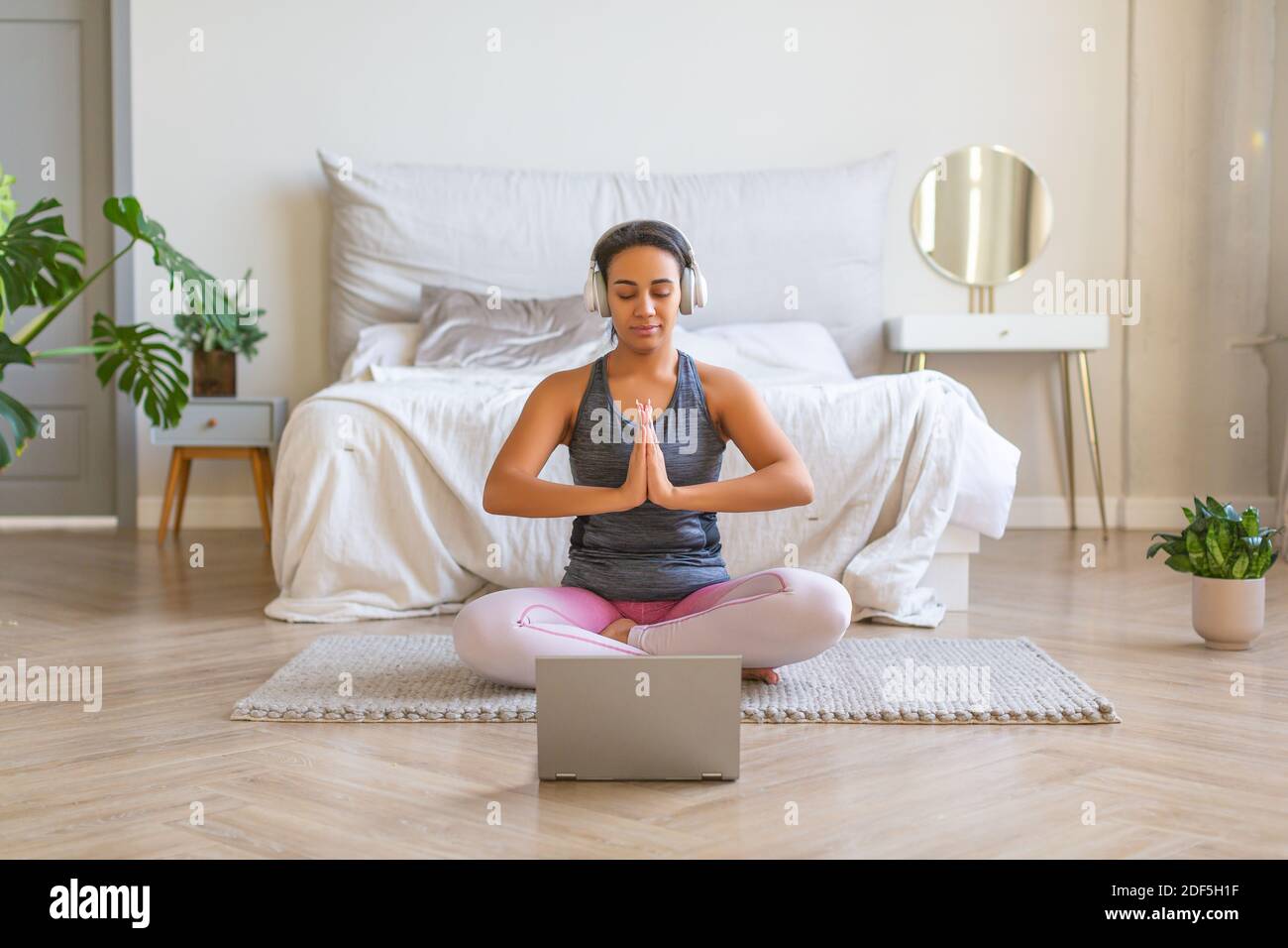 African American woman meditates at home in front of a laptop monitor. She listens to relaxing music through headphones. Stock Photo