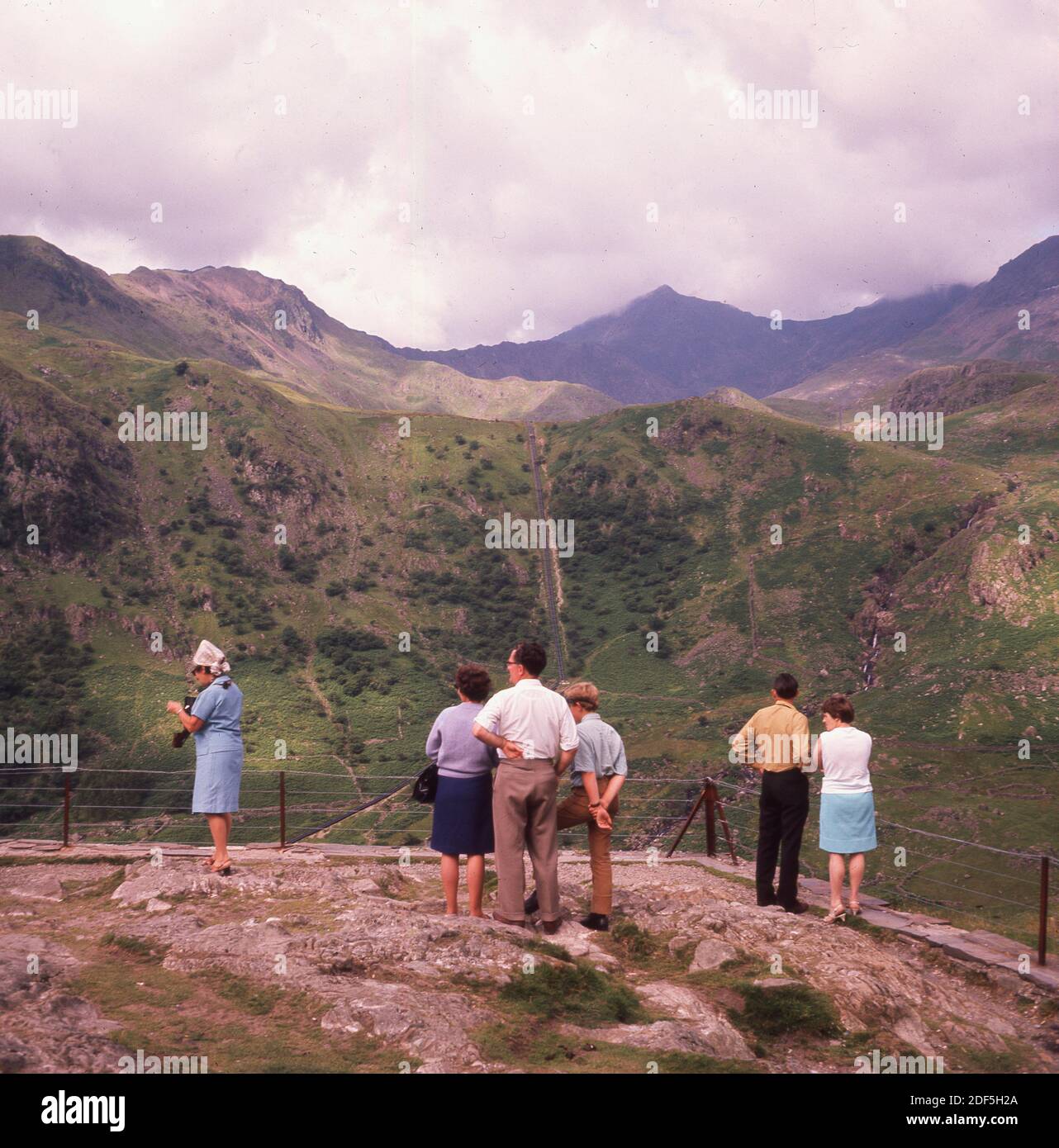 1960s, historical, Springtime and visitors high up on a vantage point on Mount Snowdon, Wales looking over the mountain range in the national park. In this era, people went to such places in normal everyday clothes, not in synthetic fleeces and mountain boots! Stock Photo