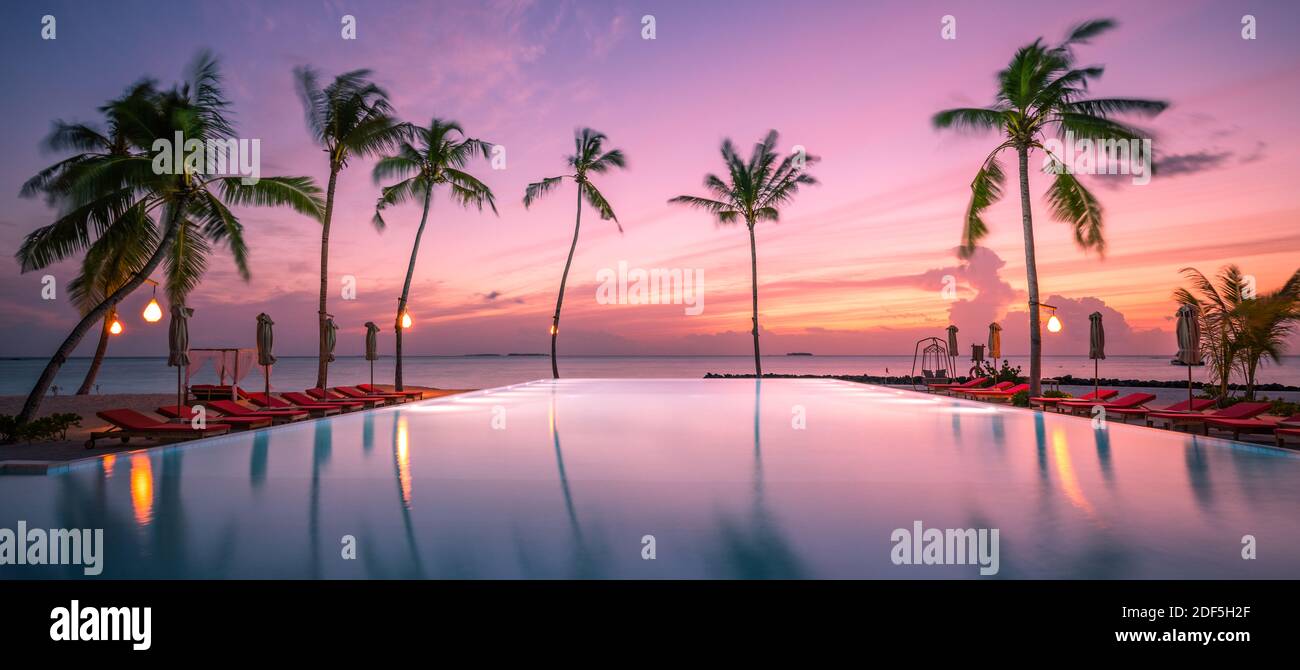 Beautiful poolside and sunset sky. Luxurious tropical beach landscape, deck chairs and loungers and water reflection. Luxury summer relax, chill vibes Stock Photo
