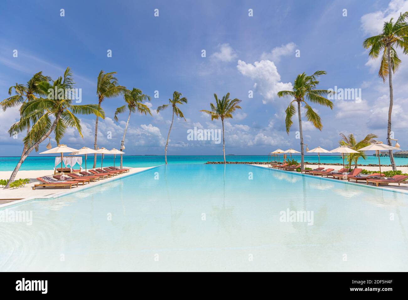 Luxury swimming pool a tropical resort. The edge luxurious swimming pool with relax deckchairs beds on the beach, infinity sea view. Inspire resort Stock Photo