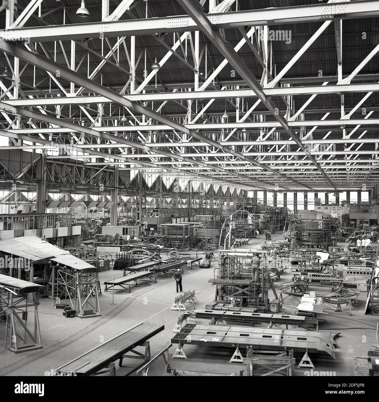 1950s, historical, overhead view inside of a giant aviation hangar showing construction of large passenger aircraft, England, UK. Picture shows the ceiling gantry structure and individual technicans on the floor, working on different sections of the airplane, including the sections of the wing. Stock Photo