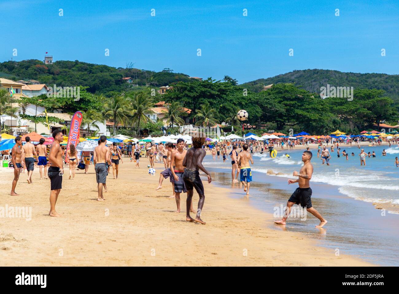 Geriba beach, Buzios, Rio de Janeiro, Brazil – December 22, 2019: Group of men having fun playing football on the beach. Lots of people around them. P Stock Photo