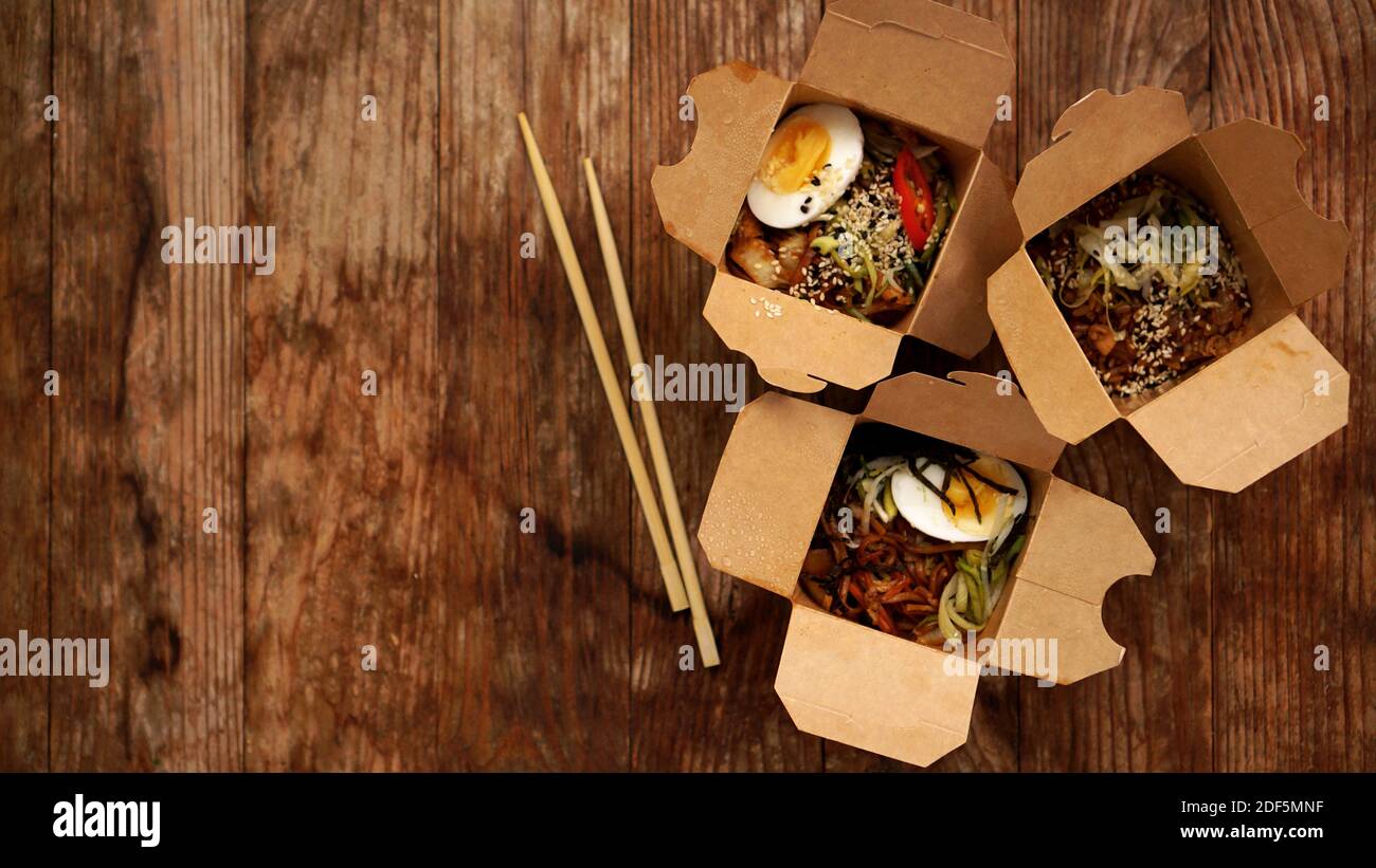 Chinese noodles with chicken and vegetables in cardboard boxes on a wooden background, Asian