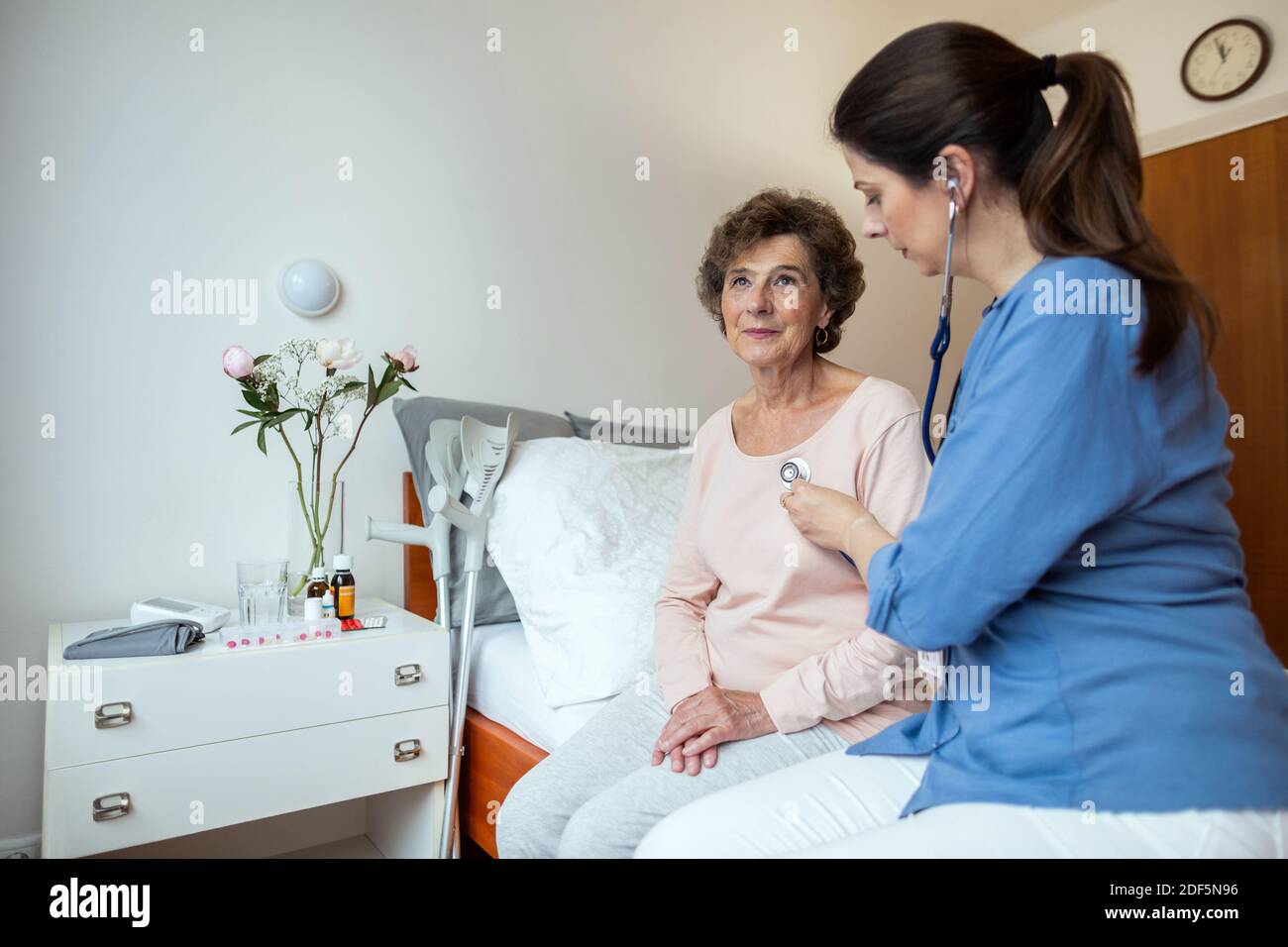 Female Doctor Listening to Lungs of Senior Patient With Stethoscope in Hospital Room. Home Nurse Listening For Breathing of Elderly Woman. Stock Photo