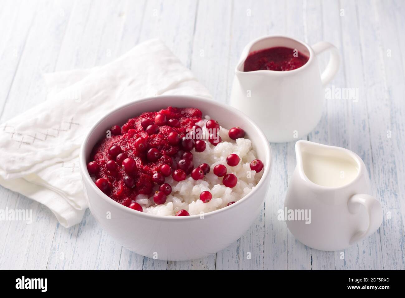 Rice pudding with cranberry jam and fresh cranberries in a white bowl on a light blue background, selective focus. Delicious traditional breakfast Stock Photo