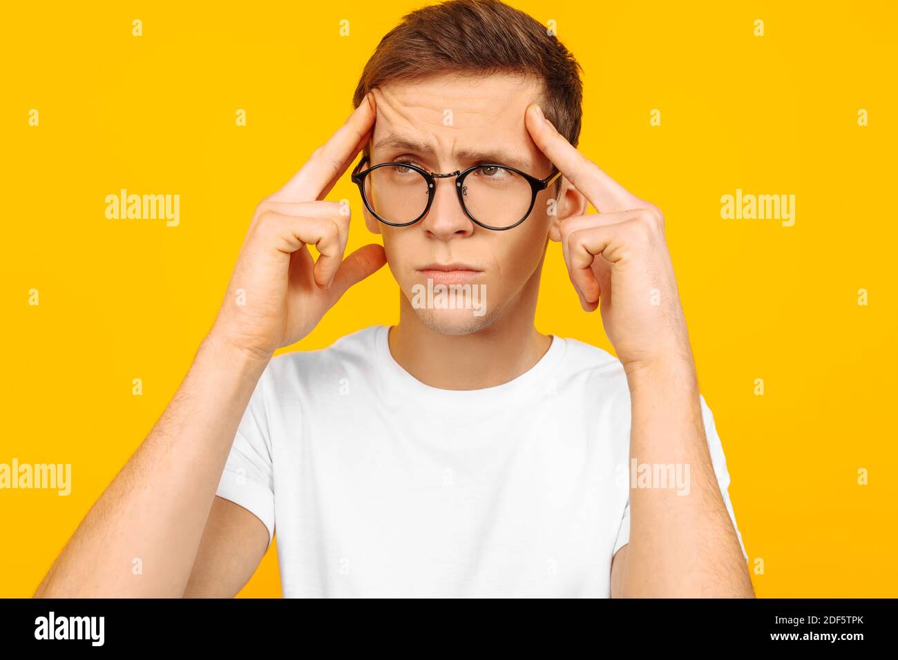 A portrait of a thoughtful dreamy guy, wearing glasses and a white T-shirt, imagines something in his mind, looks to the side, bends his lips, sinks i Stock Photo