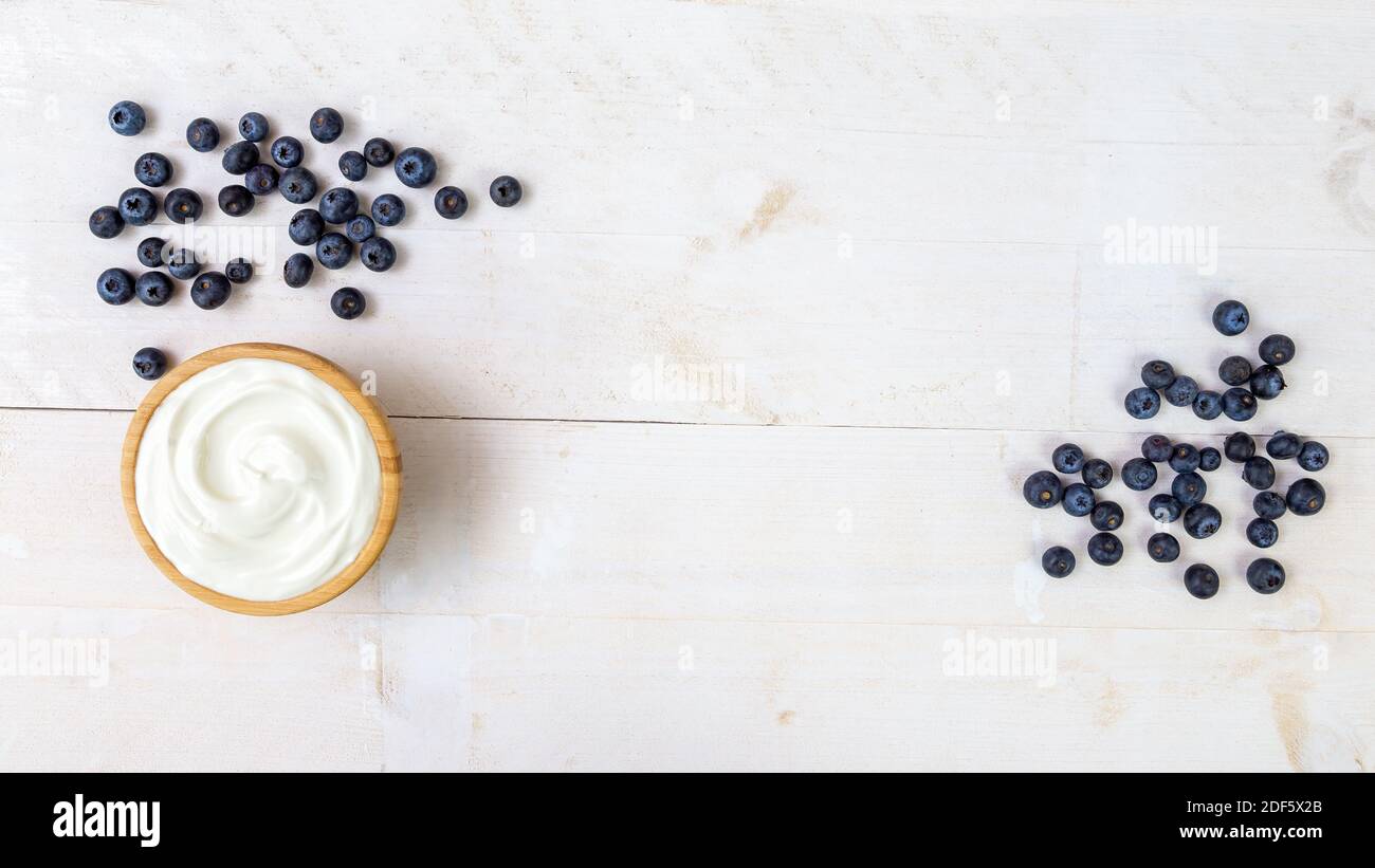 Heap of juicy blueberries and wooden bowl of smooth white yoghurt on white table Stock Photo