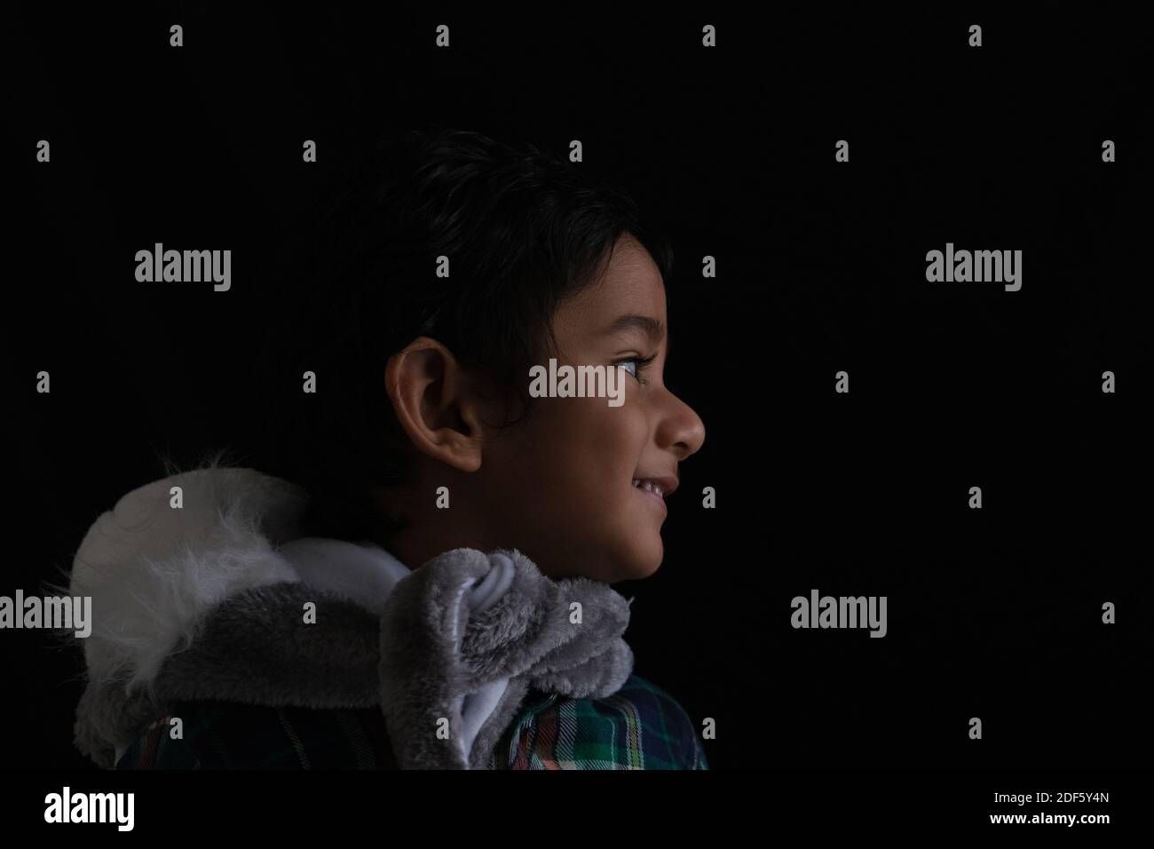 Close up portrait of Indian cute little cheerful brunette Tamil baby boy wearing casual dress and furry muffler in a black background Stock Photo