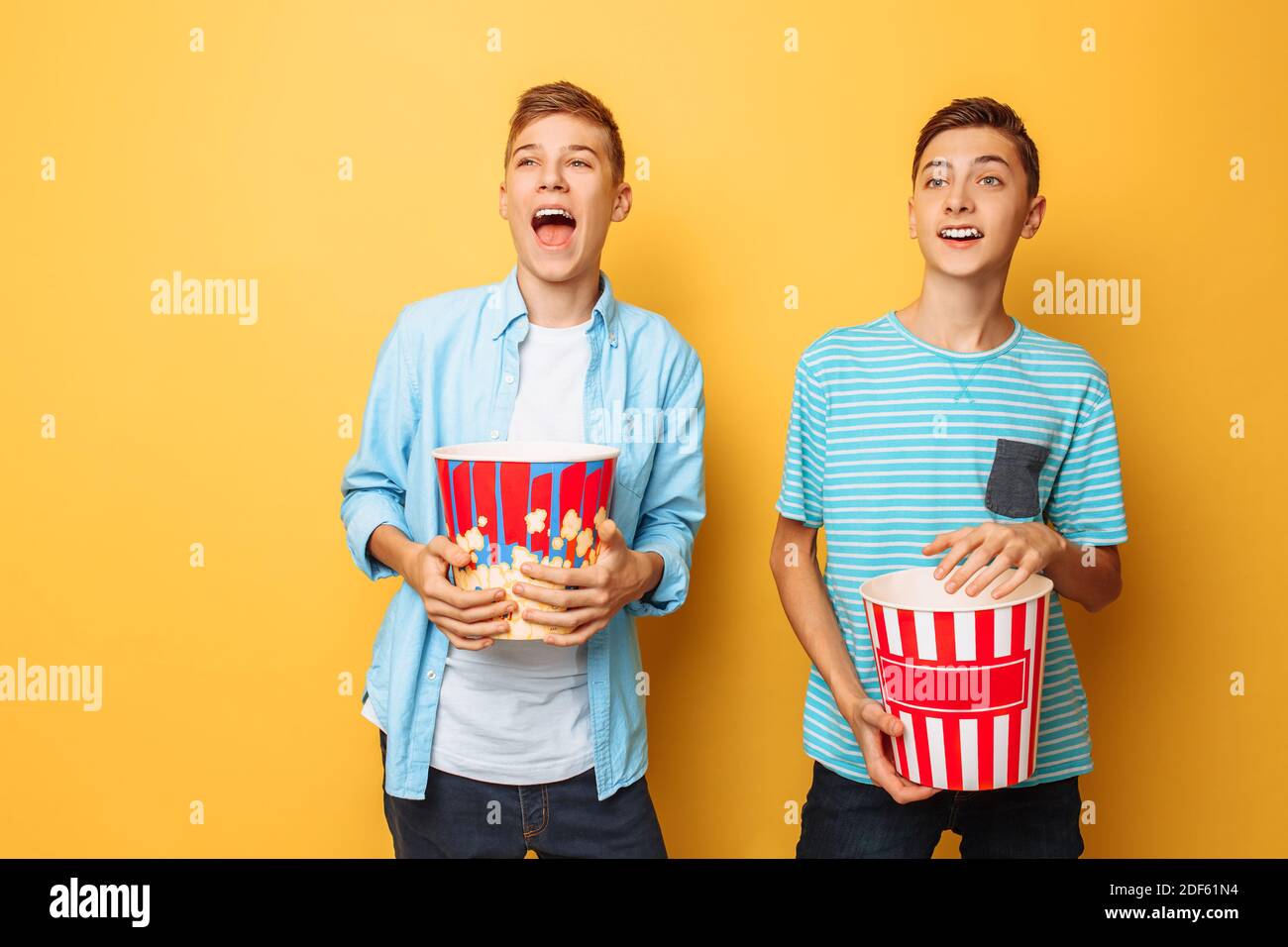 Image of two excited beautiful teenagers, guys watching an interesting movie and eating popcorn Stock Photo
