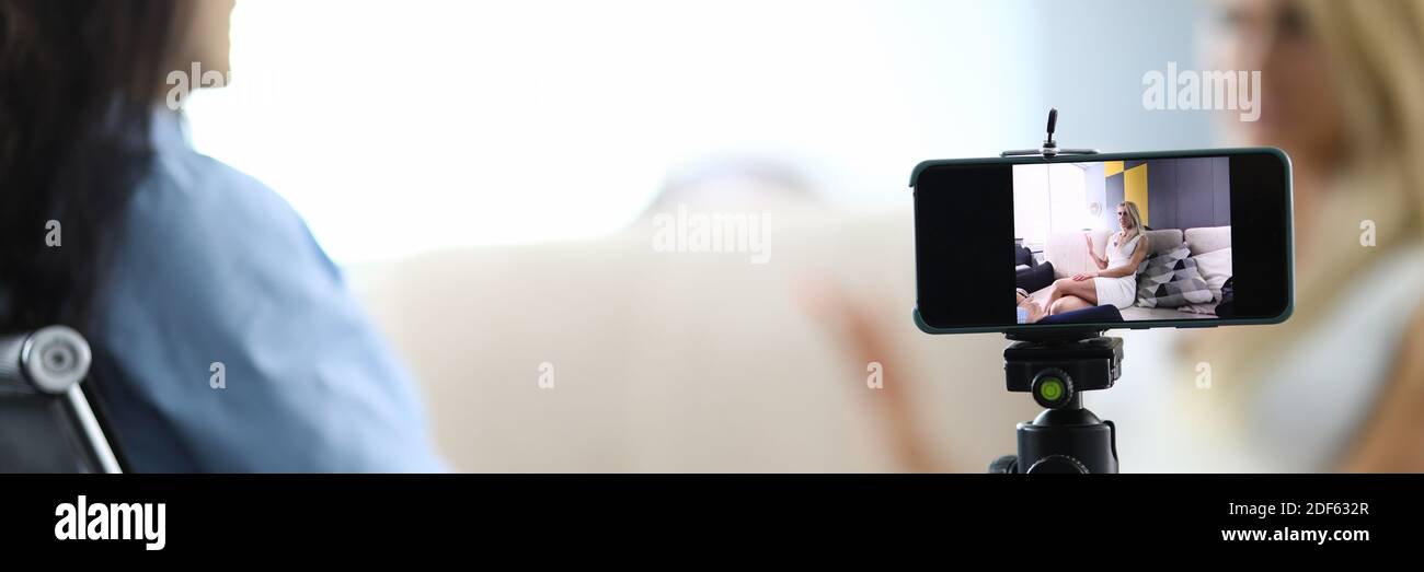 Two women sit and communicate conversation is recorded on smartphone. Stock Photo
