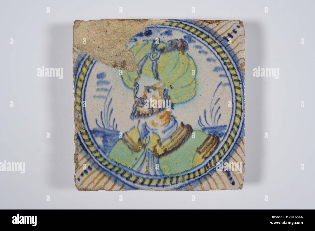 wall tile, Anonymous, 16th century, tin glaze, earthenware, General: 9.6 x 9.6 x 1.5cm (96 x 96 x 15mm), man's portrait, southern netherlands, Wall tile of earthenware covered with tin glaze. The tile is multicolored painted in blue, green, yellow and brown-orange. On the tile is a portrait of the Turkish ruler Soliman, depicted with a turban, depicted in a circular medallion with circular bands and a cable edge. The tile has a corner motif with stripes, Date1985 Stock Photo