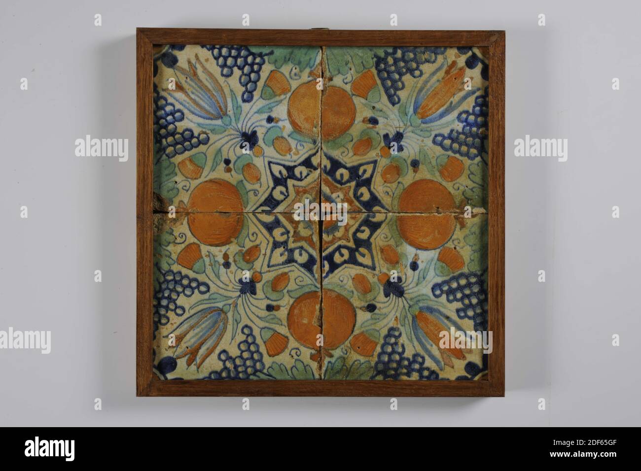 tile field, Anonymous, between 1610-1640, tin glaze, earthenware, With frame: 28.9 x 28.9 x 2.5cm (289 x 289 x 25mm), bunch of grapes, orange apple, tulip, Tile field of four tiles (two by two) of earthenware covered with tin glaze. Multicolor painted in blue, green, orange and orange brown. A star tulip is depicted on the tiles in a diagonal decor. Half an orange apple and bunch of grapes on the sides. The tiles have a star tulip and quarter rosette as corner motif, 1995 Stock Photo