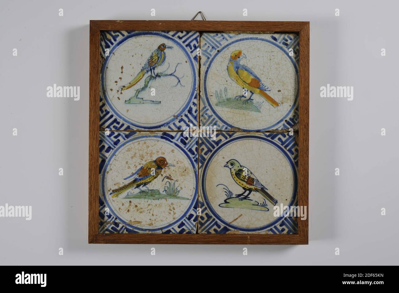 tile field, Anonymous, third quarter 17th century, tin glaze, earthenware, With frame: 28 x 27.5 x 2.5cm (280 x 275 x 25mm), bird, harlingen, Tile field of four tiles (two by two) of earthenware covered with tin glaze painted multicolored in blue, yellow, green and orange-brown. Birds are depicted within a circle on the tile field. Above left a bird with a long beak and a long tail on a branch facing right; top right a parrot-like bird facing left on a ground; Bottom left a fantasy bird on a ground pointing to the right; bottom right a tick on a ground. The tiles have a meander as a corner Stock Photo