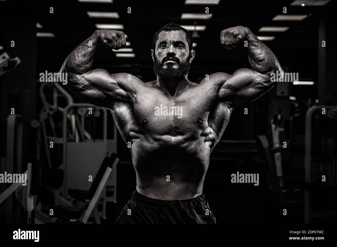 black and white of strong young bearded male showing double biceps pose in  dark night sport gym Stock Photo - Alamy