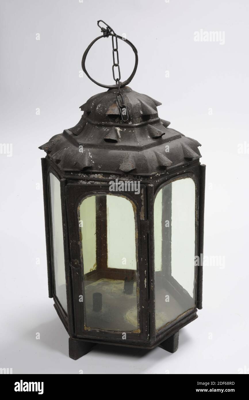 lantern, Anonymous, 18th century, wood, iron, forged, Hexagonal candle lantern made of black painted sheet iron with straight walls. The six walls, reinforced with rods at the corners, have arched windows, one of which is a hinged door. One of the windows is missing. The bottom is mounted on a wooden supporting cross and on the inside there are three cylindrical candle holders. The pagoda-shaped roof, which is profiled in three layers, has arch-shaped, round-covered ventilation holes. The bottom layer two holes per side and the two above one. On top of the lantern roof is a flat sheet iron Stock Photo