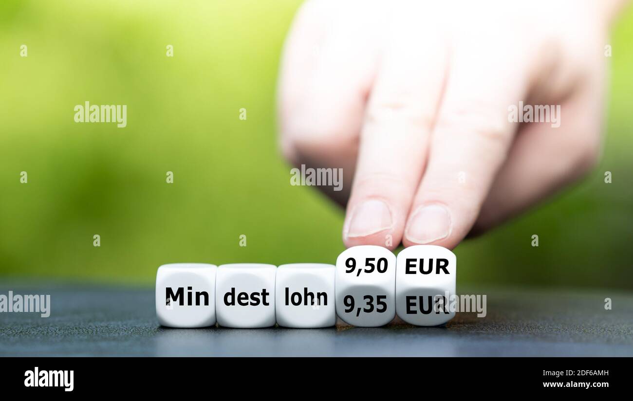 Hand turns dice and changes the German expression 'Mindestlohn 9.30 EUR' to 'Mindestlohn 9.50 EUR' (minimum wage 9.50 EUR). Stock Photo