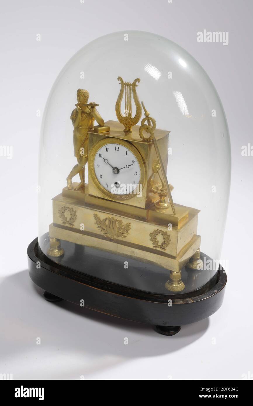 mantel clock, Anonymous, approx. 1800, glass, wood, enamel, brass, Total: 36 x 26 x 15.8cm 360 x 260 x 158mm, Bell: 30.8 x 23.5 x 13.8cm 308 x 235 x 138mm, Base: 6 x 26 x 15.8cm 60 x 260 x 158mm, flute, music making, lyre, Empire fire-gilded brass mantel clock under glass bell jar. On the right side of the clock a boy playing a flute in a short tunic leans, on top of the clock a four-stringed lyre, on the left a long staff with two wreaths and a lion's head with a bowl underneath. The clock and figures are on a beam with three wreaths on the front, the middle of which contains a harp. The Stock Photo