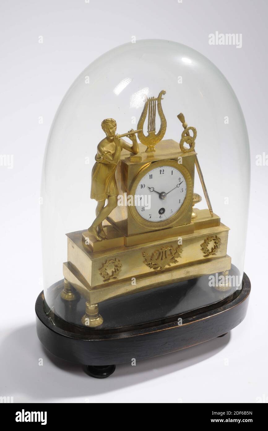 mantel clock, Anonymous, approx. 1800, glass, wood, enamel, brass, Total: 36 x 26 x 15.8cm 360 x 260 x 158mm, Bell: 30.8 x 23.5 x 13.8cm 308 x 235 x 138mm, Base: 6 x 26 x 15.8cm 60 x 260 x 158mm, flute, music making, lyre, Empire fire-gilded brass mantel clock under glass bell jar. On the right side of the clock a boy playing a flute in a short tunic leans, on top of the clock a four-stringed lyre, on the left a long staff with two wreaths and a lion's head with a bowl underneath. The clock and figures are on a beam with three wreaths on the front, the middle of which contains a harp. The Stock Photo
