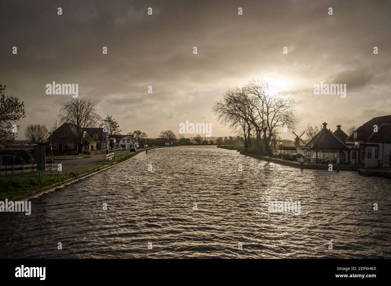 Dramatic light over Vliet canal and surrounding polder landscape with houses and a windmill near Voorschoten, The Netherlands Stock Photo