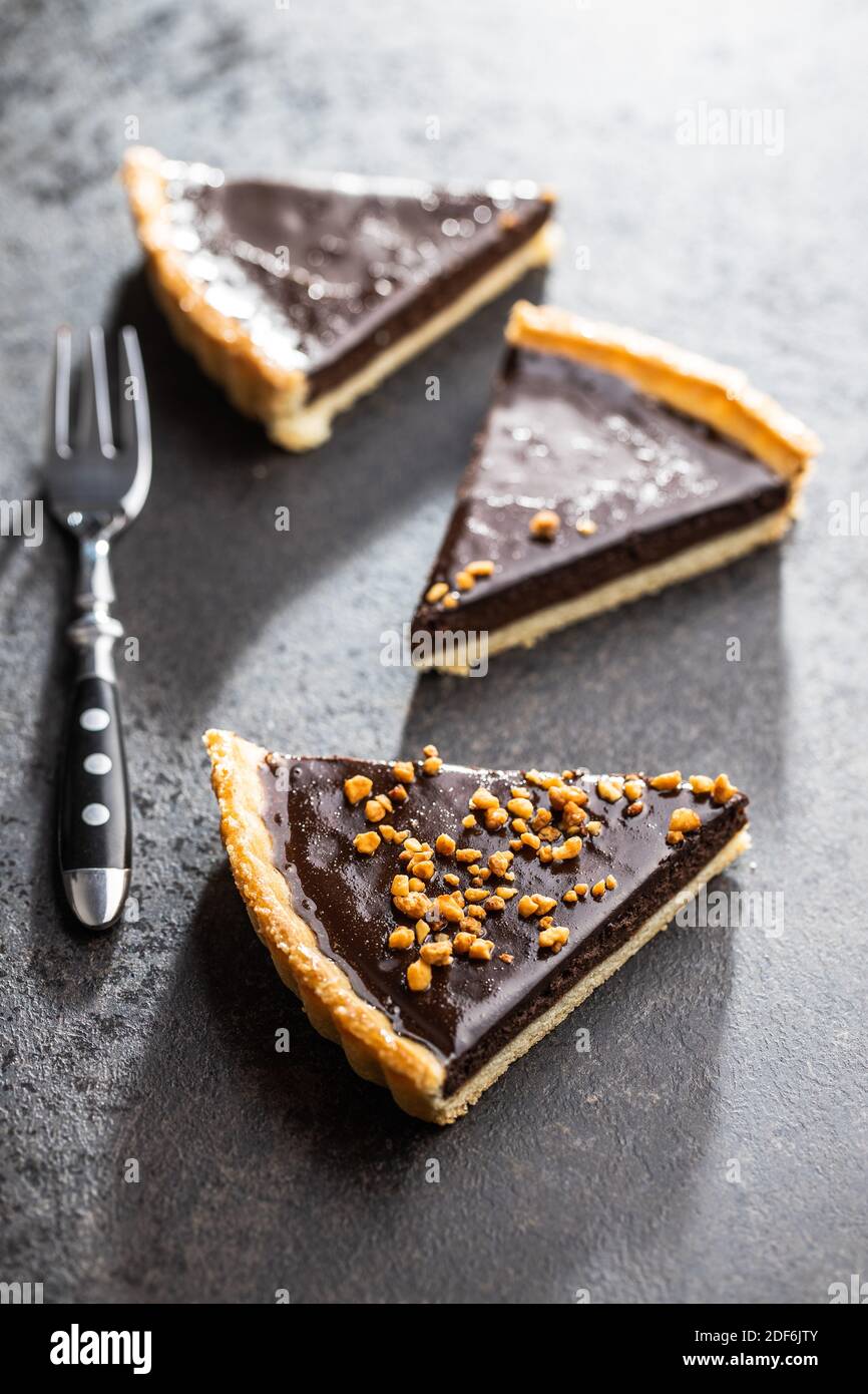 Sweet chocolate pie with crushed nuts on black table. Stock Photo