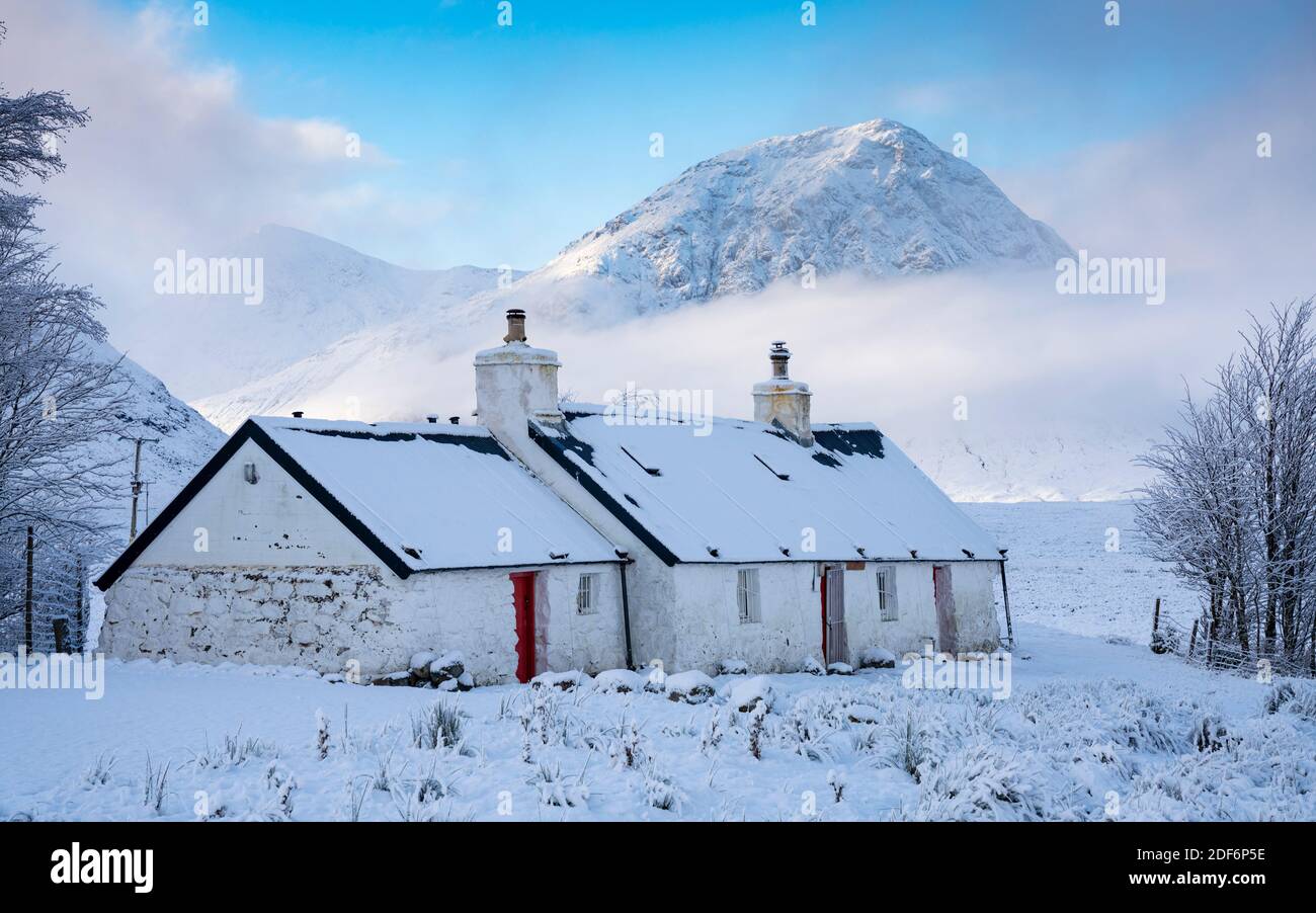 Glen Coe, Scotland, UK. 3 December 2020. A cold front has brought the first snowfall to the Scottish Highlands. Rannoch Moor and Glen Coe are covered in several inches of snow. Bright sunshine throughout the day created beautiful winter landscapes.  Pictured; Blackrock Cottage with mist covered Buachaille Etive Mor in the distance.  Iain Masterton/Alamy Live News Stock Photo