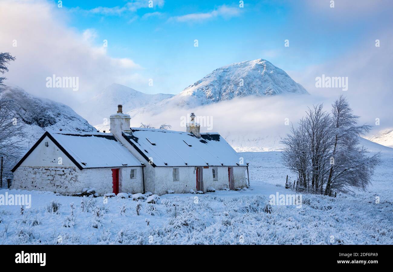 Glen Coe, Scotland, UK. 3 December 2020. A cold front has brought the first snowfall to the Scottish Highlands. Rannoch Moor and Glen Coe are covered in several inches of snow. Bright sunshine throughout the day created beautiful winter landscapes.  Pictured; Blackrock Cottage with mist covered Buachaille Etive Mor in the distance.  Iain Masterton/Alamy Live News Stock Photo