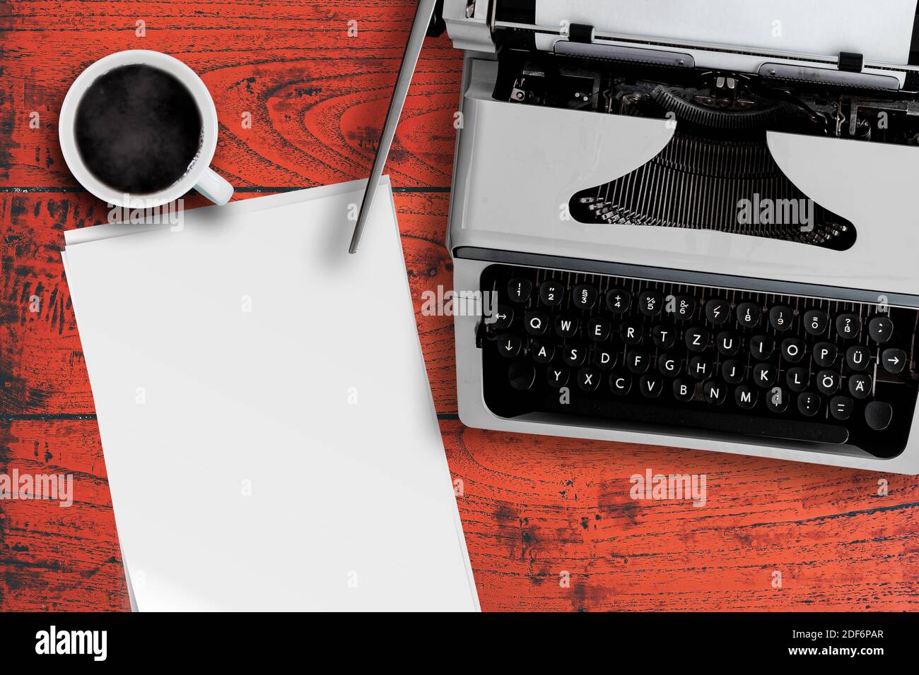 directly above view of old typewriter, cup of steaming hot coffee and stack of blank writing paper on red wooden desk Stock Photo
