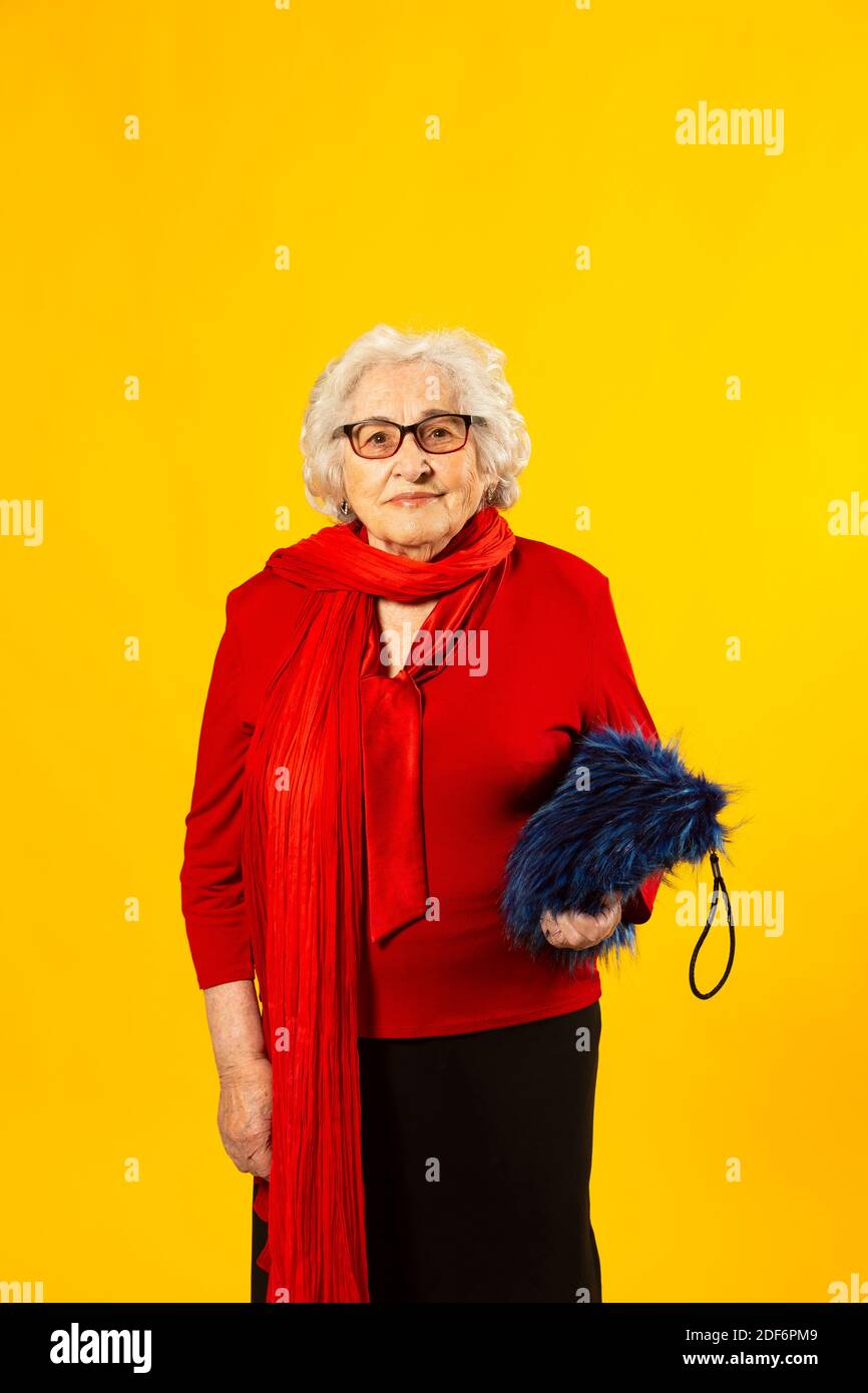 Studio portrait of a senior woman wearing a red shirt and a blue hairy bag, against a yellow background Stock Photo