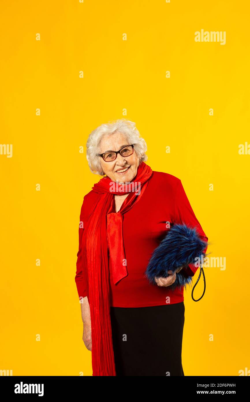 Studio portrait of a senior woman wearing a red shirt and a blue hairy bag, against a yellow background Stock Photo