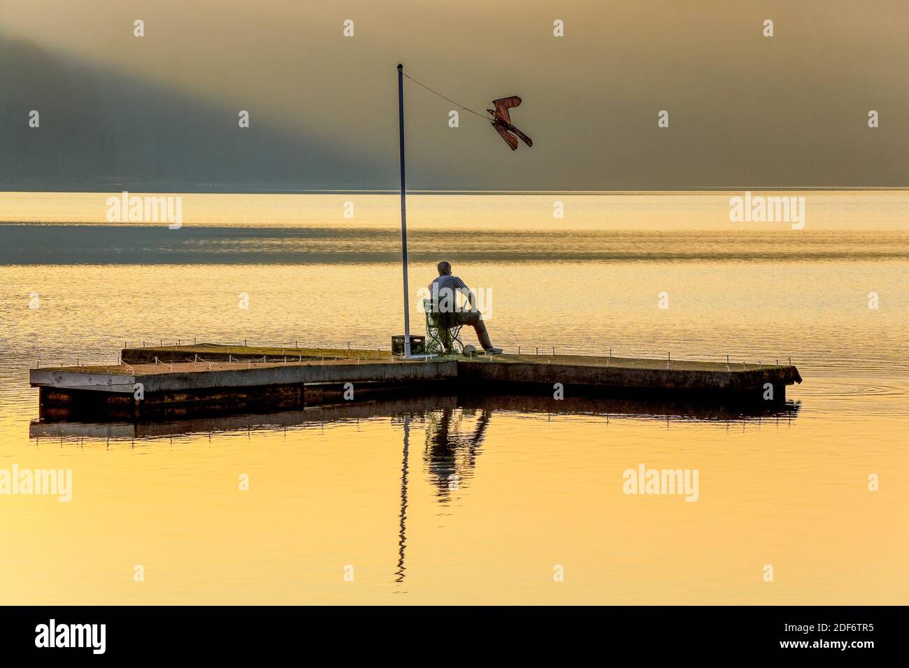 An almost lifelike fisherman sits on the wooden plateau and looks out over the Dieksee, Malente, Germany. The bird Stock Photo