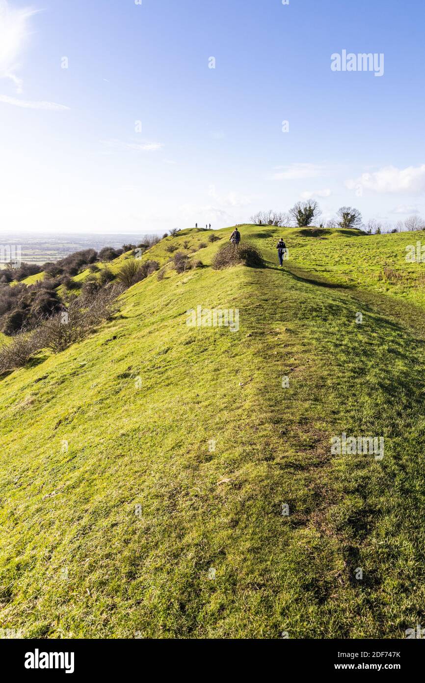 Hikers walking along the rampart of a slight univallate Iron Age hillfort on Ring Hill at the Cotswold viewpoint of Haresfield Beacon, Gloucestershire Stock Photo